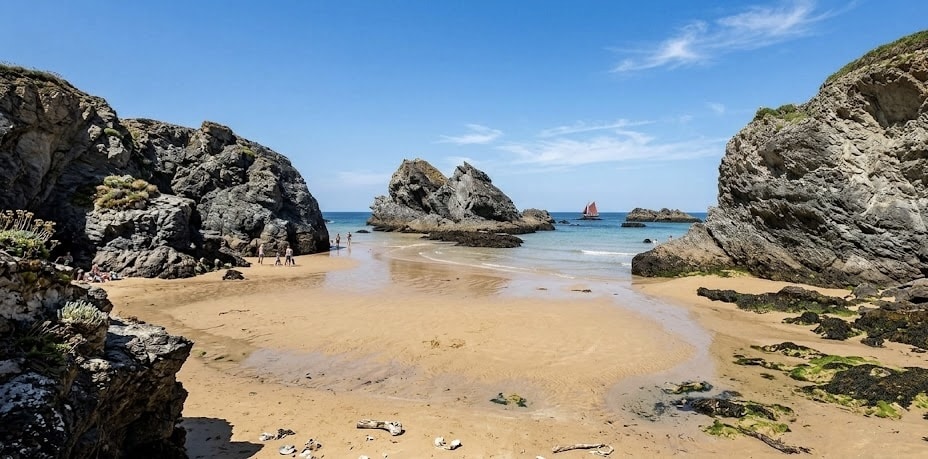 Crique de sable entre les rochers avec un vieux gréement au large, dans le Morbihan